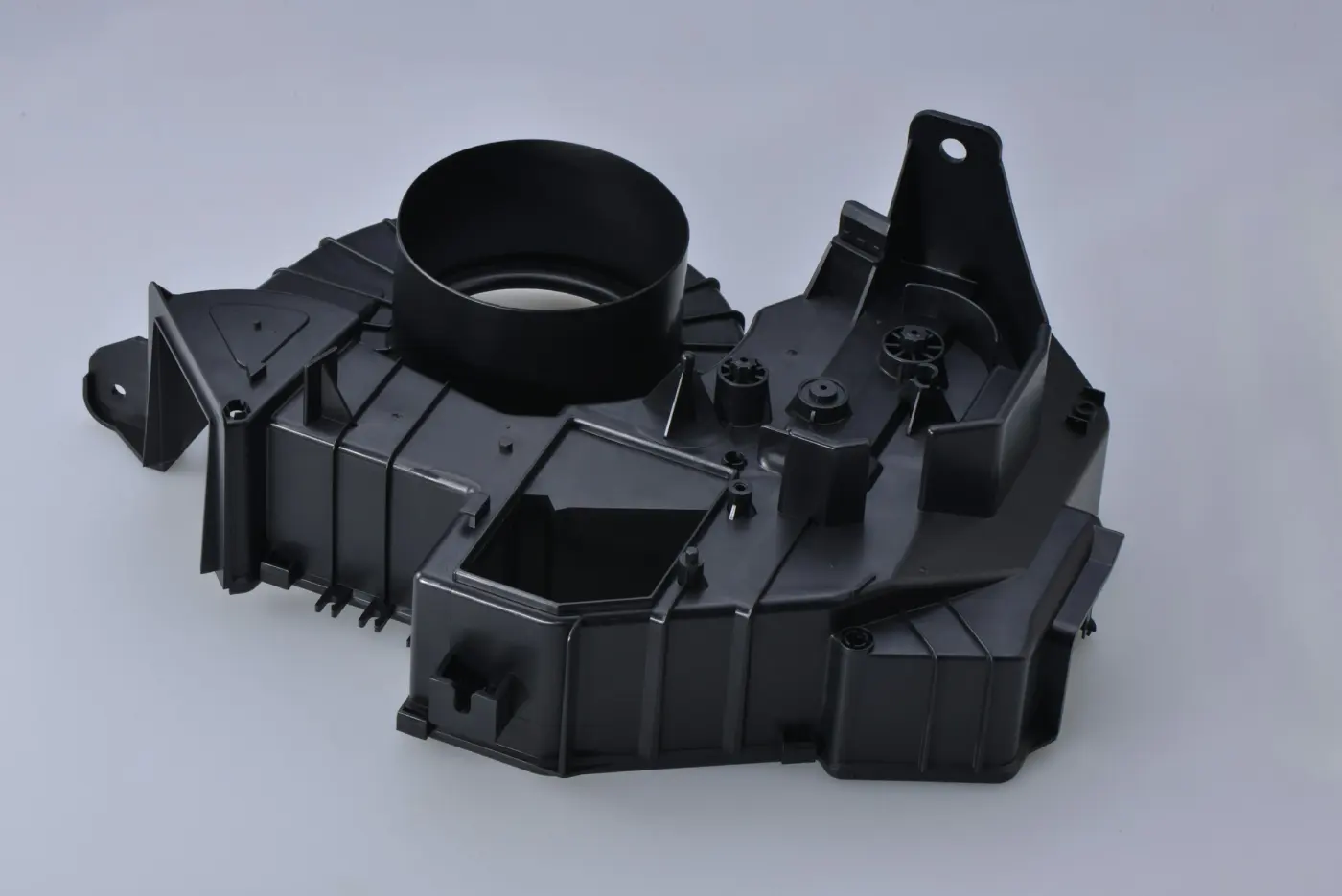 Complex black molded plastic housing with a round outlet and mounting tabs